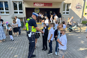 zdjęcie przedstawia policjanta rozdającego odblaski dzieciom