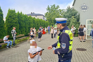 zdjęcie przedstawia policjanta rozdającego odblaski dzieciom