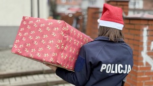 zdjęcie przedstawia policjanta niosącego paczkę dla potrzebującej rodziny