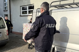 zdjęcie przedstawia policjanta niosącego paczkę dla potrzebującej rodziny