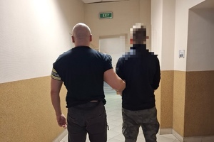 na zdjęciu policjant prowadzący zatrzymanego