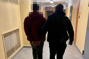 zdjęcie przedstawia policjanta doprowadzającego zatrzymanego